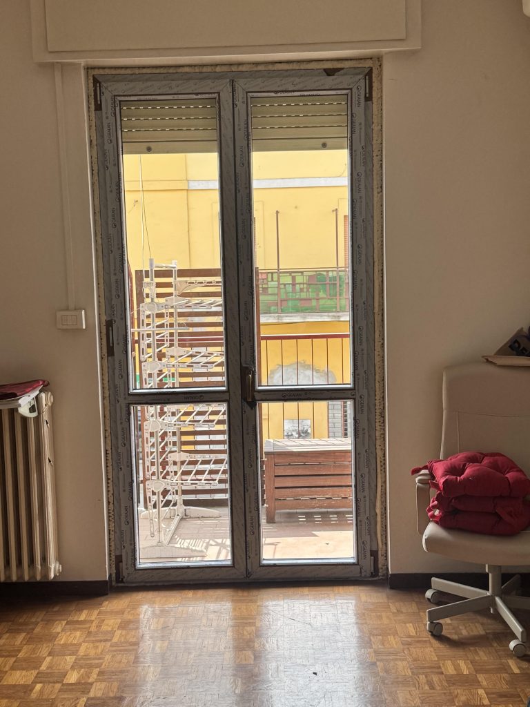 Porta finestra in PVC a due ante durante la posa, con schiuma visibile tra telaio e muratura